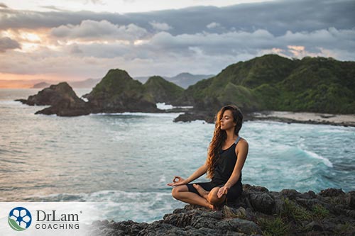 An image of a woman meditating on a rocky shoreline