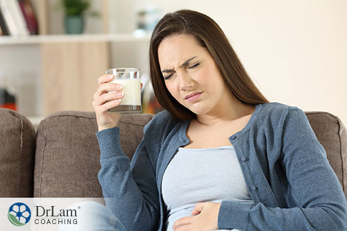 An image of a woman with a glass of milk grimacing and holding her stomach