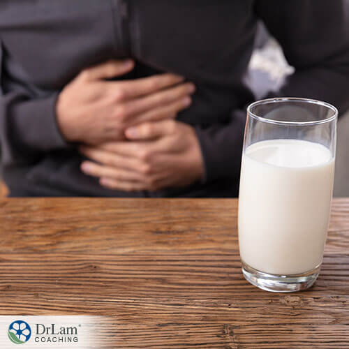 An image of a glass of milk with a man in the background holding his stomach