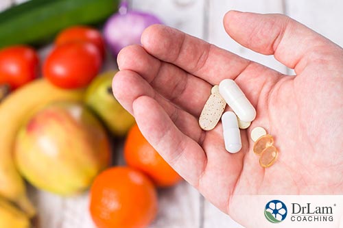 An image of different supplements being held in the palm of a hand with fresh fruit in the background