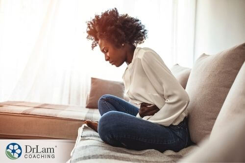 An image of a woman almost crouching in pain on the couch