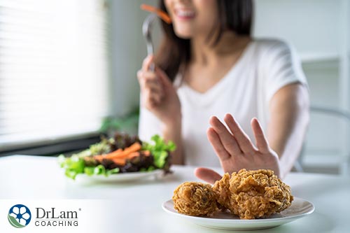 An image of a woman pushing a plate of fried chicken away as she eats a salad