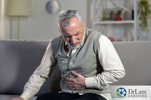 An image of an older man holding his abdomen in discomfort while sitting on the couch