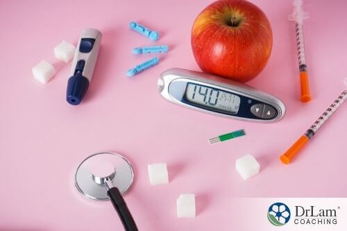 An image of a glucometer, sugar cubes, apples, and a stethoscope scattered on a pink surface