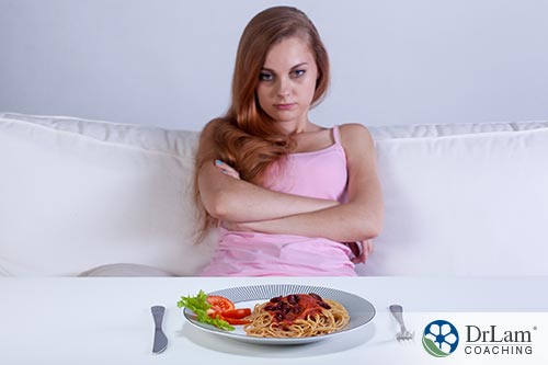 An image of a woman sitting with her arms crossed while she looks at a plate of untouched food