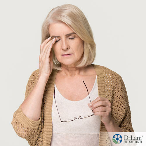 An image of an older woman rubbing her eyes and holding her glasses