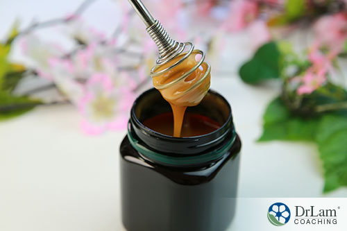 An image of a honey dipper in a dark jar of manuka honey