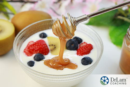 An image of a honey dipper drizzling manuka honey into a small bowl of yogurt with some berries