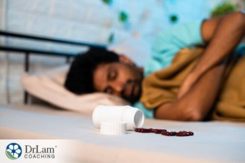 An image of a spilled bottle of pills next to a sleeping man