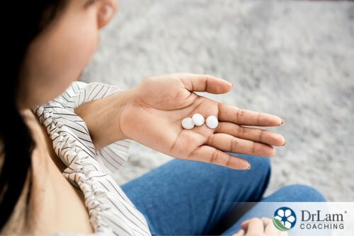 An image of a woman holding three white pills