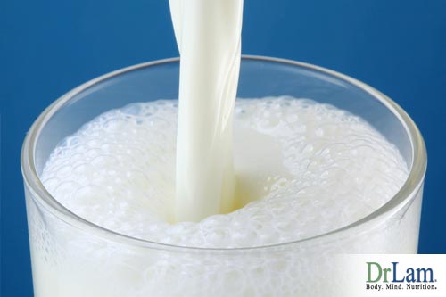 View of the top of a glass cup with milk being poured in and developing a slight froth. Milk may inhibit stomach enzyme release making it more difficult to digest other foods in the food combining diet.