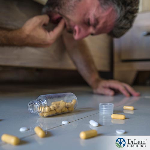 An image of a man leaning over to the floor with his fingers in his mouth and pills spilled all around