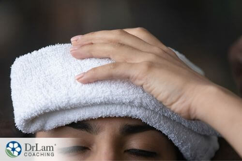 An image of a woman holding a warm washcloth on her forehead
