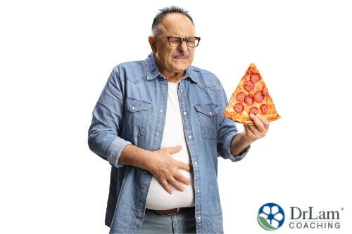 An image of an older man holding a slice of pepperoni pizza and his gut in pain