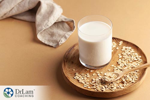 An image of a glass of oat milk on a wood saucer with a wooden spoon and oats spread around
