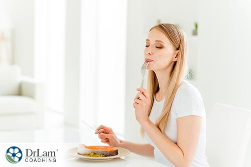An image of a woman eating a bite of baked salmon