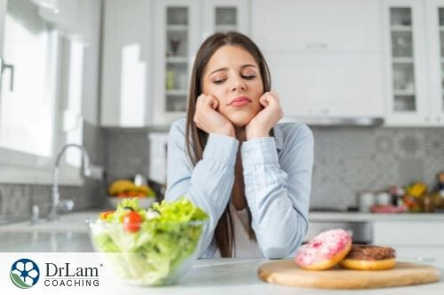 An image of a stressed-out woman choosing between eating a salad and doughnuts