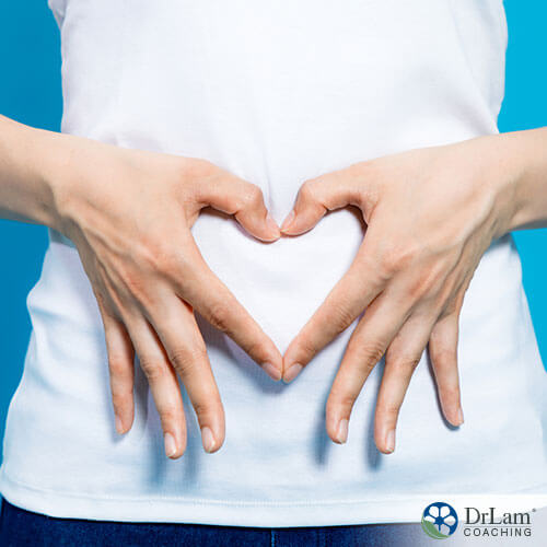 An image of a woman making a heart shape with her hands over her gut area