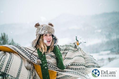 An image of a woman smiling in the snow wearing a big scarf and hat to keep warm