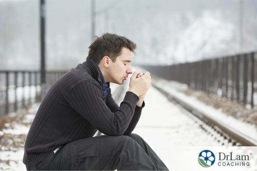 An image of a depressed man sitting on the train tracks