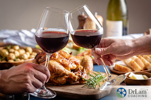 An image of two people toasting with glasses of red wine with a roasted chicken dinner in the background