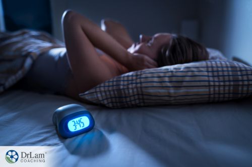 An image of a woman in bed holding her ears and an alarm clock showing the time is three forty-five in the morning