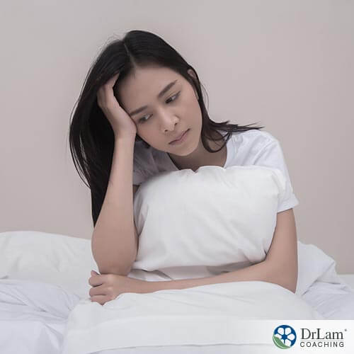 An image of a sad young woman holding her head and a pillow