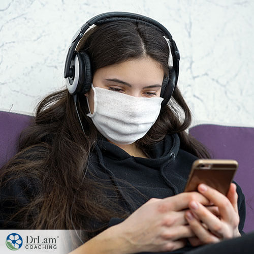 An image of a teen wearing a mask and headphones looking at her phone
