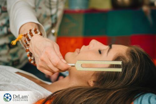 An image of a woman laying down with a tuning fork next to her