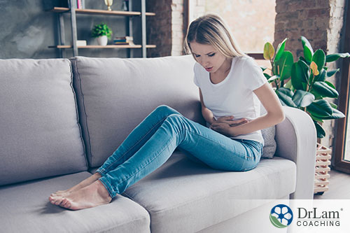 An image of a young woman on the couch holding her abdomen in pain