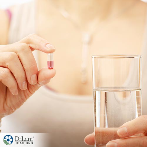 An image of a woman holding a capsule and glass of water