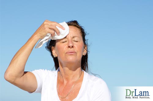 A woman in the sun wiping sweat off her brow and looking overheated, a possible sign of adrenal fatigue symptoms