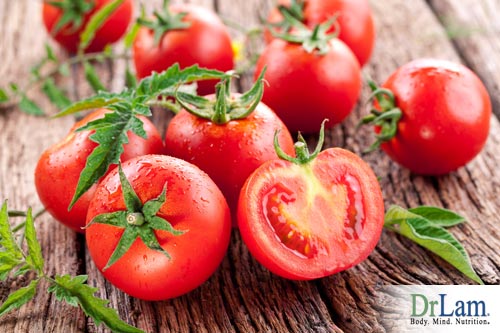 Several tomatoes, one of them cut in half, on a rough wooden surface like a wooden table. Acidic foods like tomatoes can neutralize digestive enzymes in the mouth, with consequences for what else you can eat in the food combining diet.