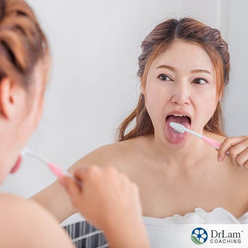 An image of a young woman brushing her tongue in the mirror