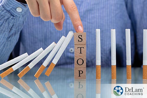 An image of a line of cigarettes stacked like dominos toppling over with the word stop in the center keeping the second half from falling
