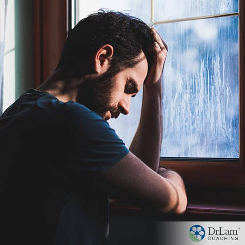 An image of a depressed man holding his head next to a window
