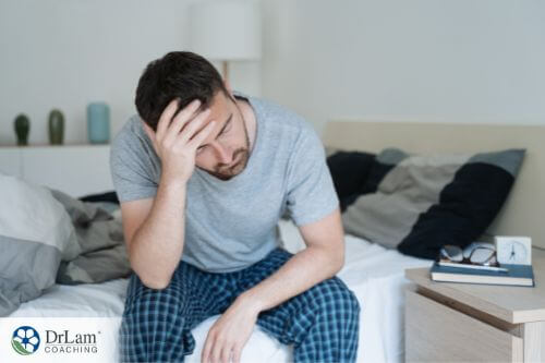 An image of a man sitting on his bed holding his head in pain
