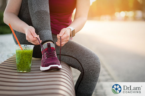 An image of a woman tying her sneakers with a green drink next to her