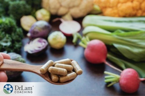 An image of a spoonful of supplement capsules with various vegetables in the background