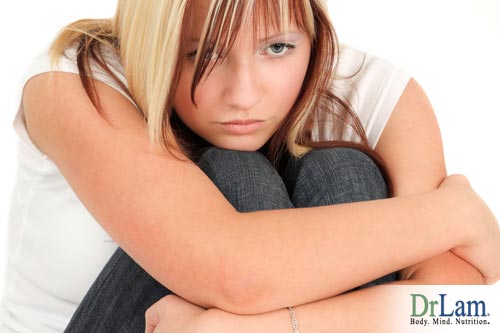 A girl hugging her knees and looking disaffected. She may be suffering from depression and adrenal fatigue.